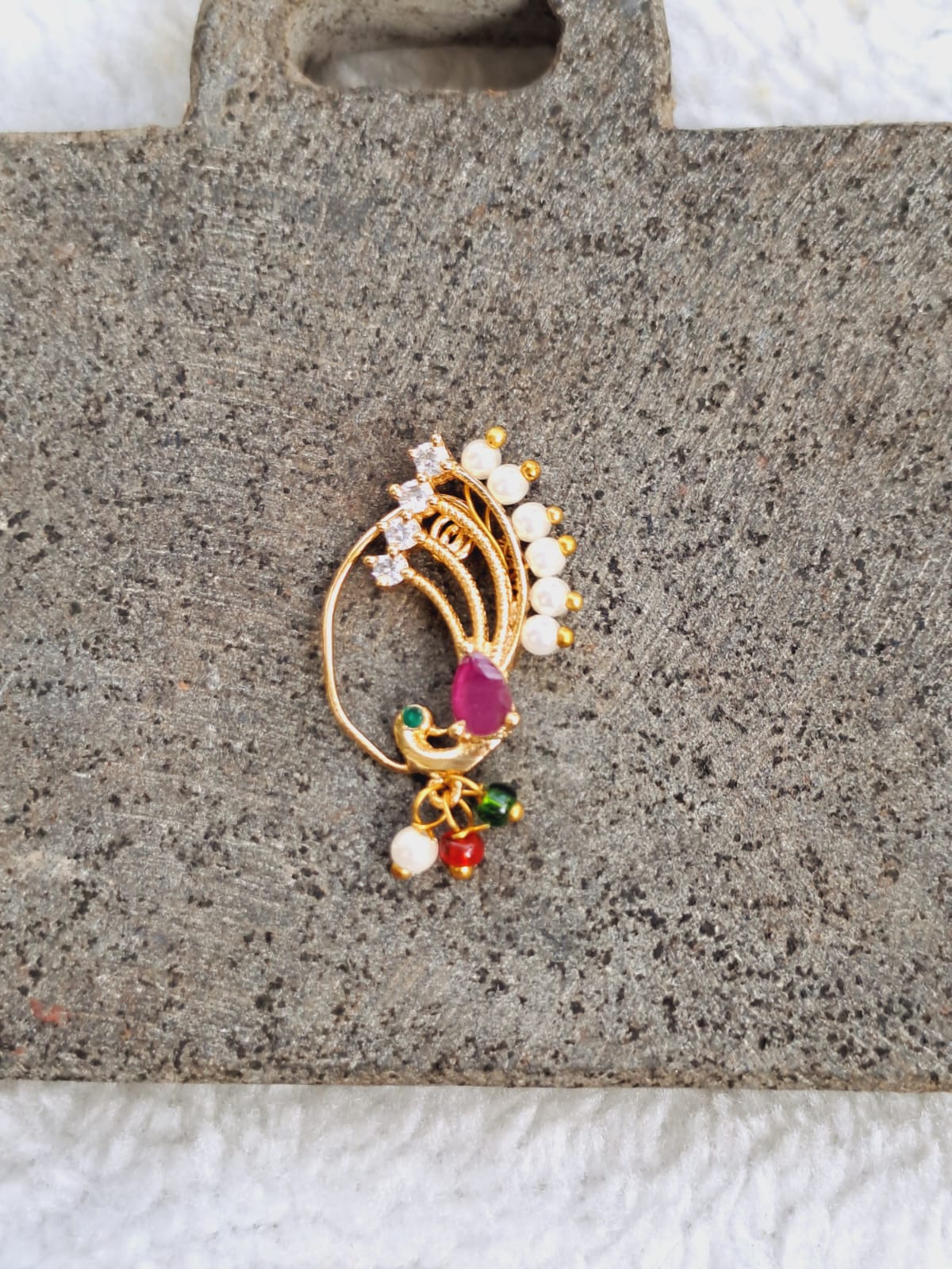 Opulent Dancing Peacock Nath - Ornate gold-toned brooch with colorful jewel-encrusted peacock design, featured on a textured beige fabric background.