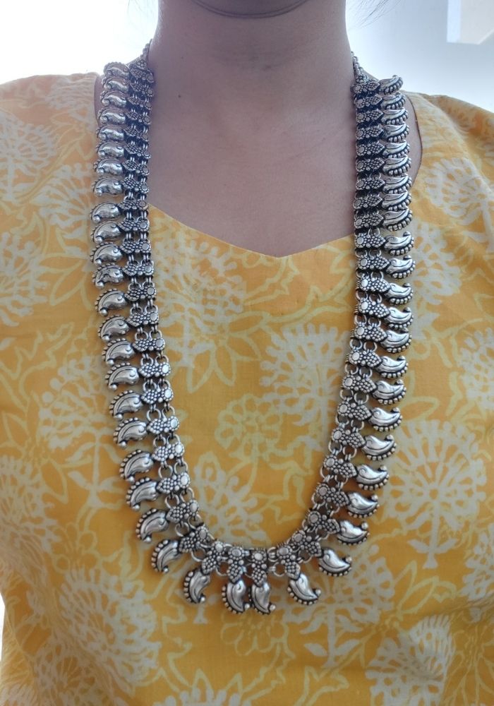 Elegant oxidized silver-toned beaded necklace with intricate floral design, displayed against a vibrant yellow patterned background.