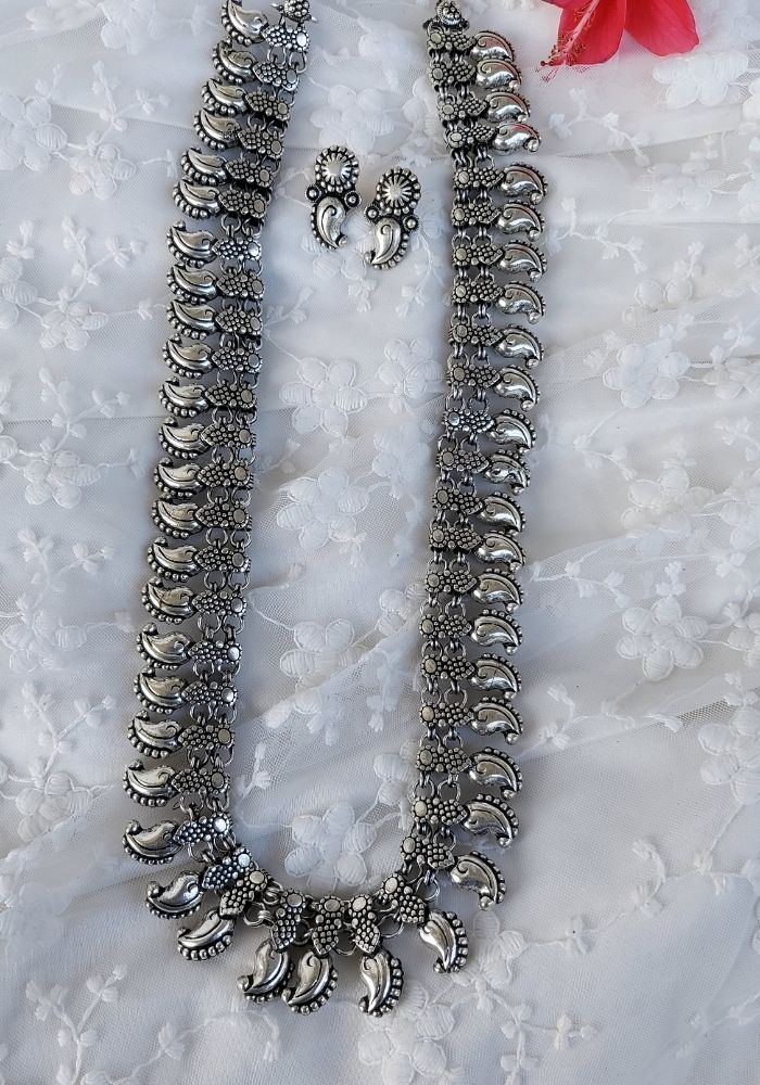 Intricate oxidised metal necklace and earrings from Mugdha Jewellery Store, featuring crescent-shaped pendants and detailed floral designs.