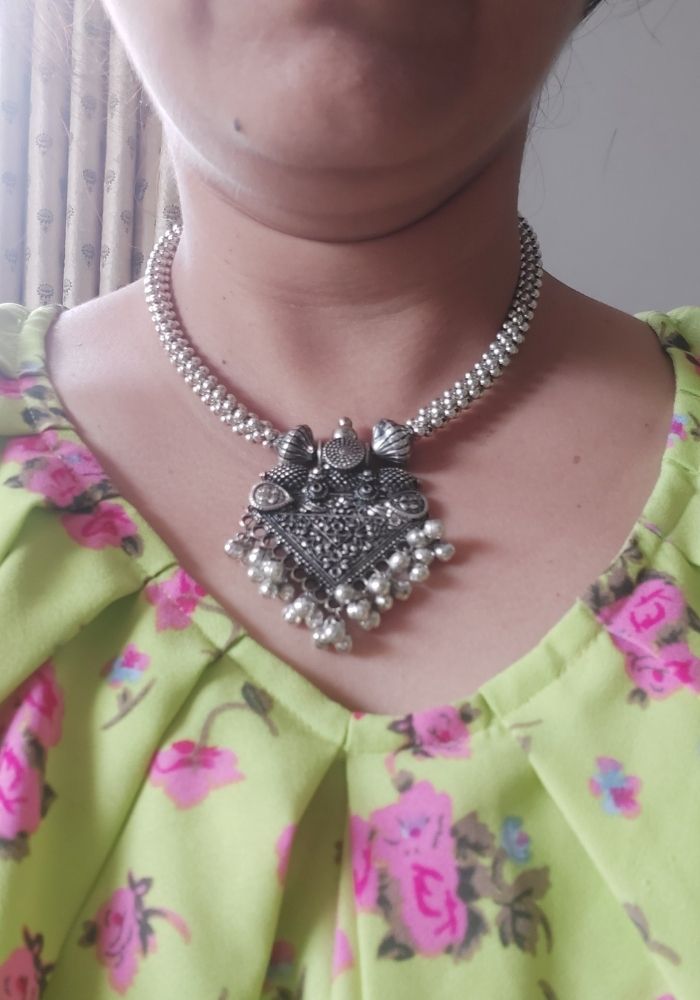 Ornate oxidised silver temple pendant necklace adorned with elegant floral motif, against a vibrant yellow and pink floral patterned dress.