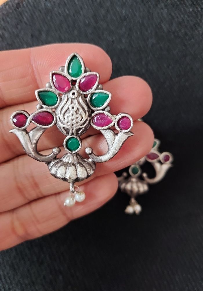 Ornate multicolored designer earrings with oxidized silver finish and intricate floral motif, showcased on a hand.