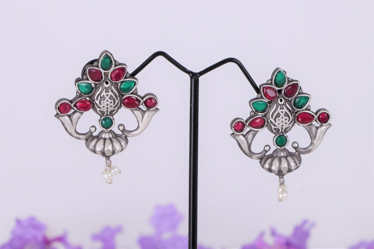 Multicolour designer oxidised earrings from Mugdha Jewellery Store. The image shows a pair of elegant earrings featuring a mix of red, green, and silver-toned gemstones arranged in a floral pattern. The earrings have a vintage, oxidised metal finish and are accented with delicate pearls.