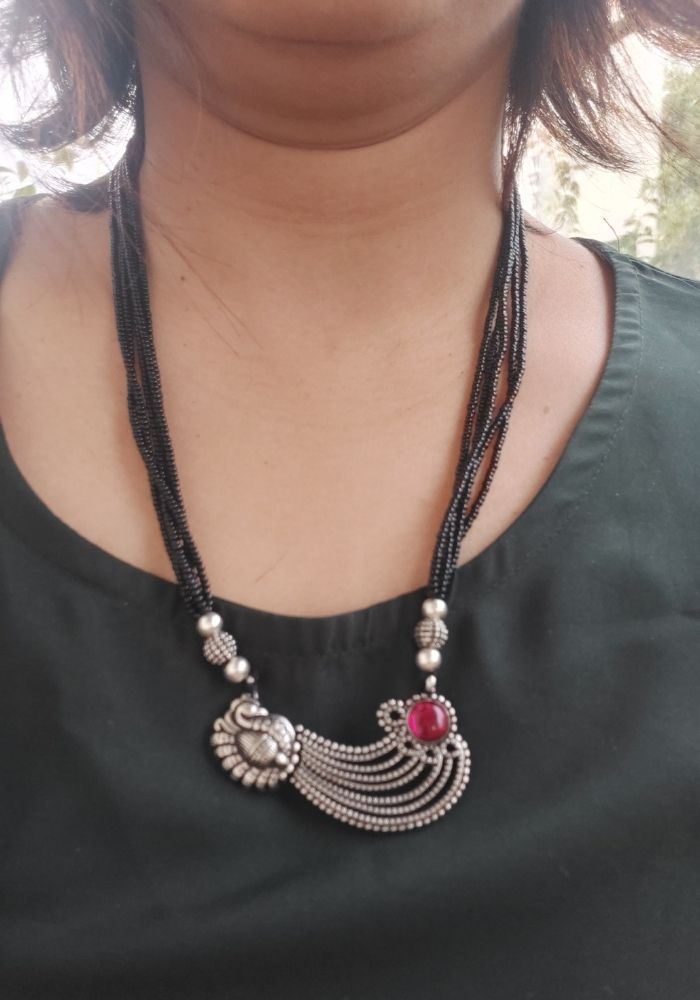 Elegant oxidized silver necklace with intricate floral design and vibrant red stone accent, worn by a woman against a dark background.