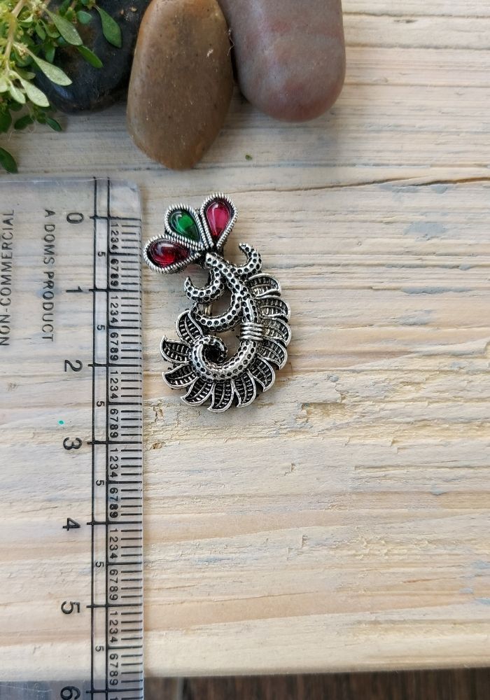 Oxidized metal nose pin with intricate floral design and colorful gemstones, displayed on a wooden surface with measurement scale.