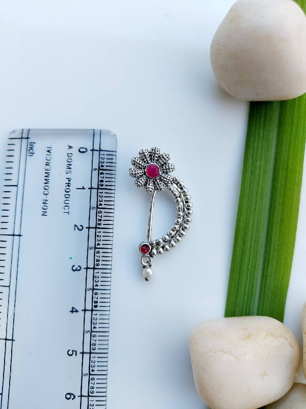 Exquisite flower-shaped oxidized nath on measurement scale, showcasing intricate metalwork and vibrant ruby accents against a minimalist white and green backdrop.