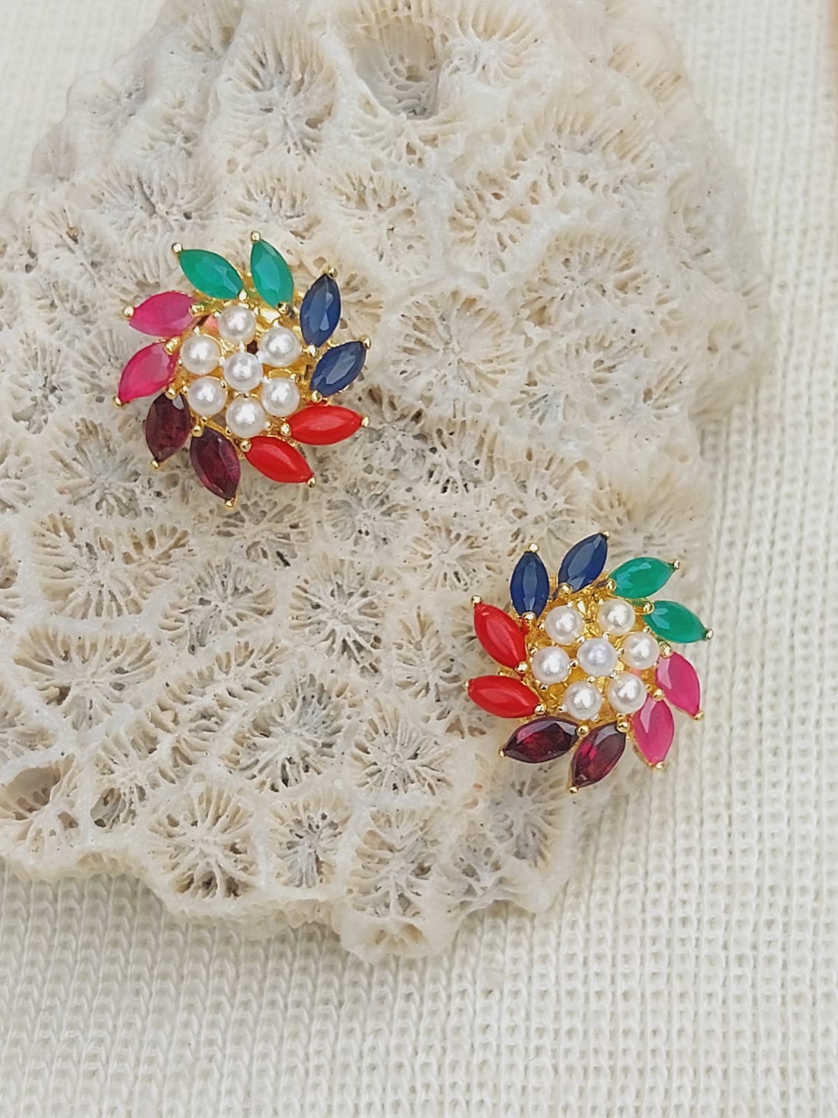 Multicolored gemstone and pearl pendant set on a white lace background from the Mugdha Jewellery Store.