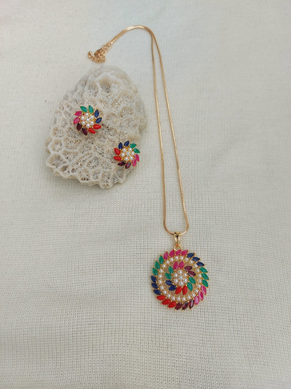 Ornate Navratna Pendant Set with Delicate Lace Accent, Vibrant Gemstone Detailing, and Shimmering Gold Chain, Displayed on Soft Ivory Background