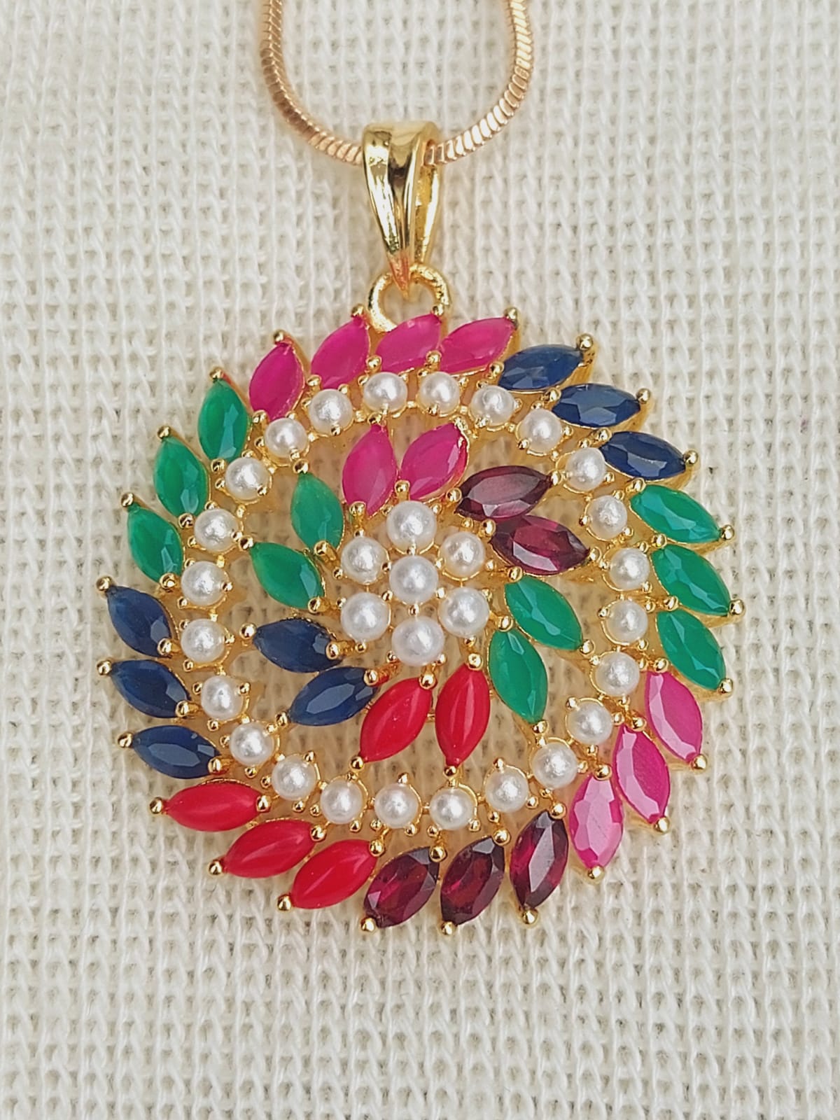 Multicolored gemstone pendant necklace with pearl accents in a spiral design, displayed on a light-colored textured background.