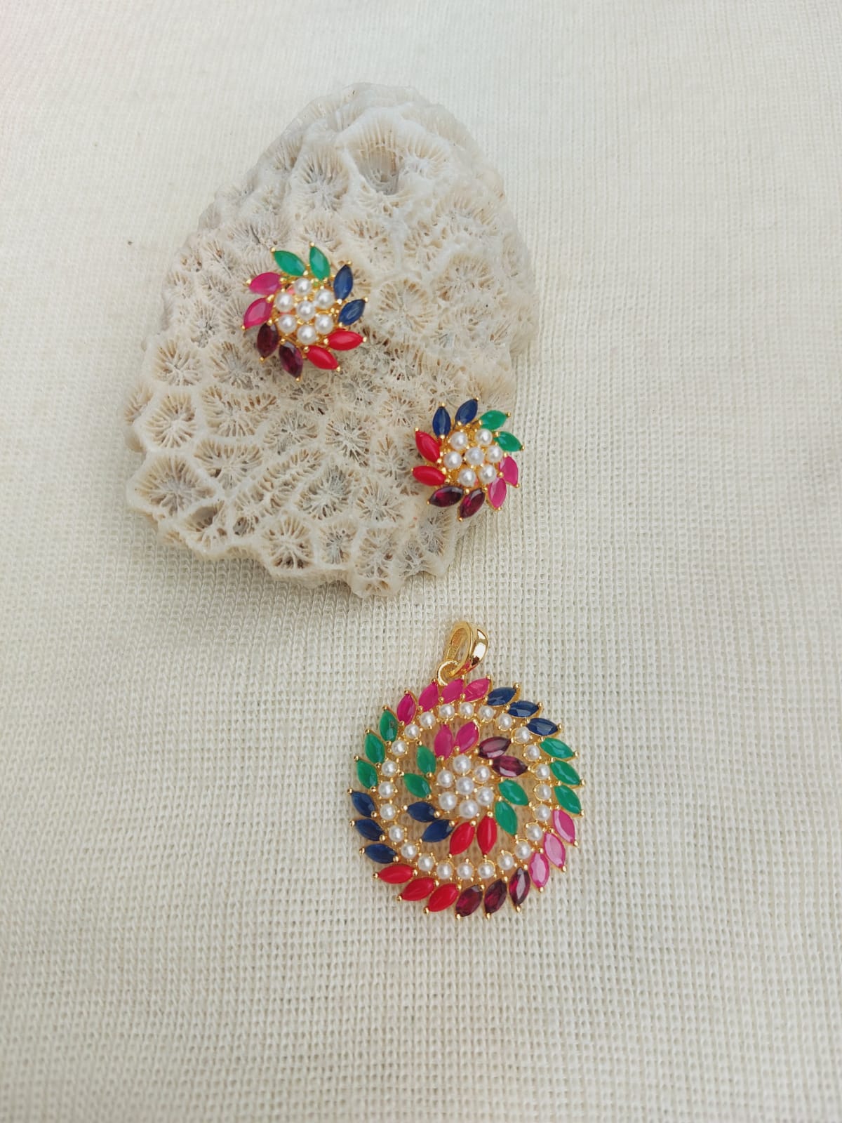 Colorful jeweled pendant and earrings displayed on textured fabric surface