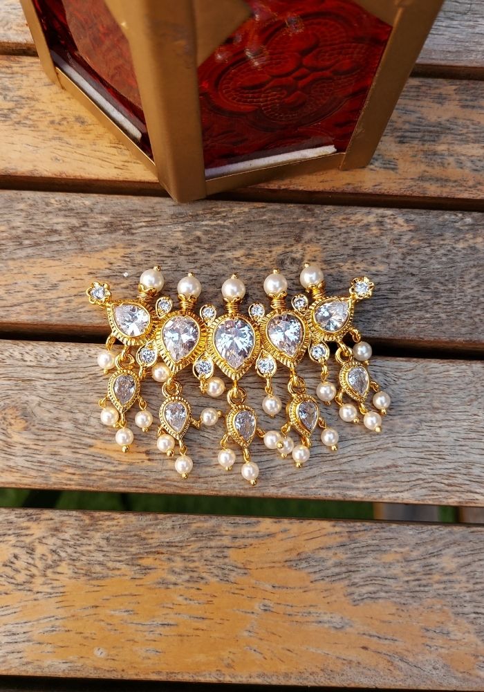 Elegant gold-plated pendant with sparkling crystal accents and intricate design, displayed on a wooden surface.