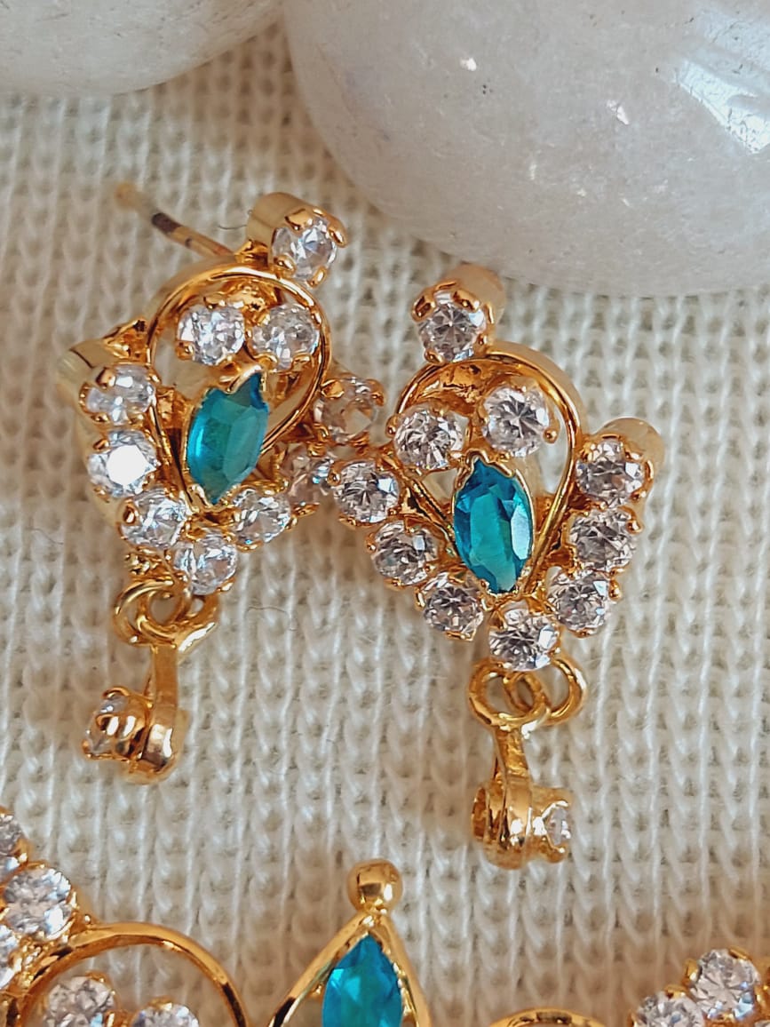 Elegant gold-toned pendant set with white and blue stones, displayed on a textured background.