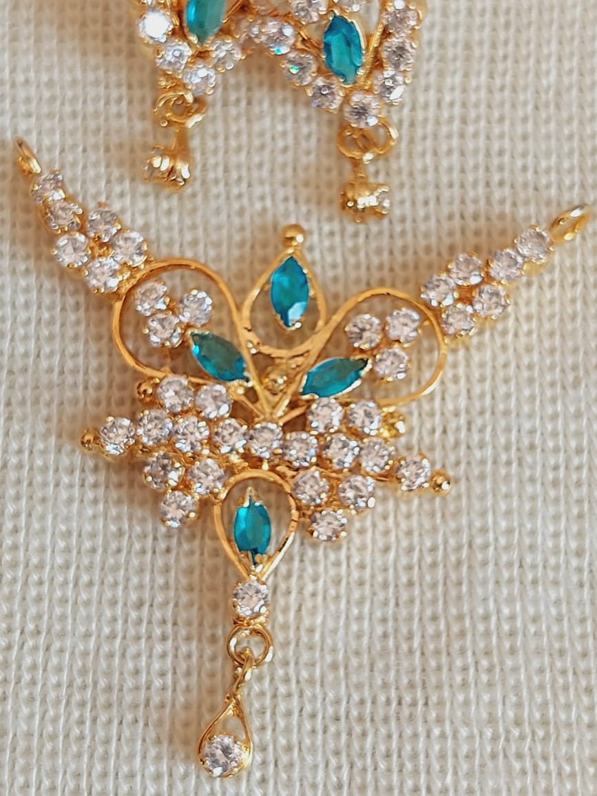 Elegant gold-toned pendant set with sparkling white and blue stones arranged in a floral design. The detailed ornament features intricate metalwork and shimmering accents, creating a visually striking and high-quality piece of jewelry.