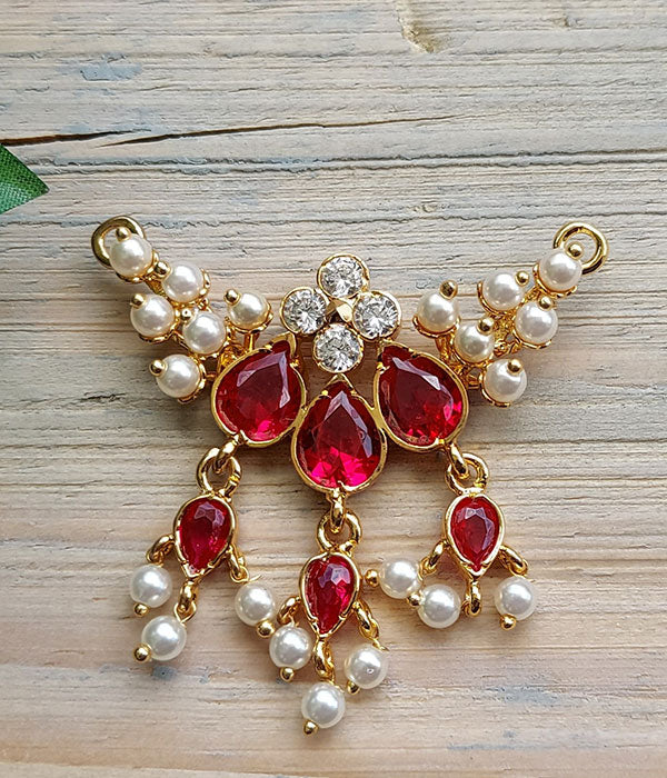 Elegant gold-toned Karwari Draksha Tanmani pendant featuring vibrant red gemstones, dazzling rhinestones, and delicate pearl accents on a wooden background from Mugdha Jewellery Store.