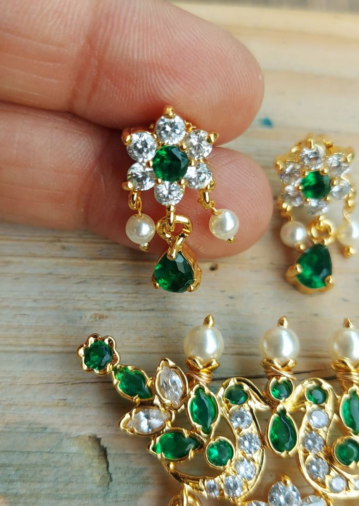 Elegant emerald and diamond flower-shaped tanmani pendant with pearl accents, displayed on a wooden surface.