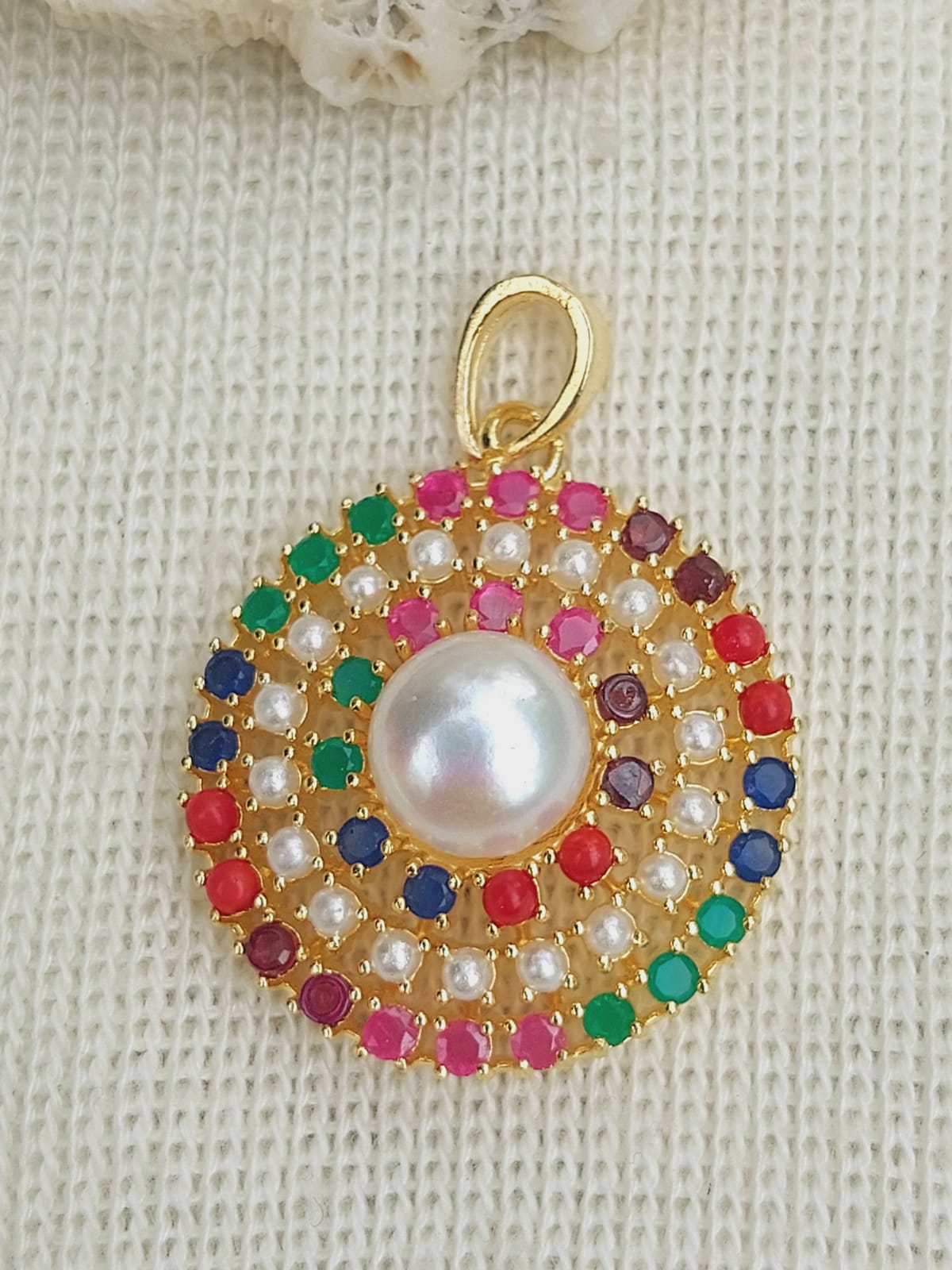 Colorful gemstone pendant with a central pearl, set in a gold-toned frame on a textured white background.