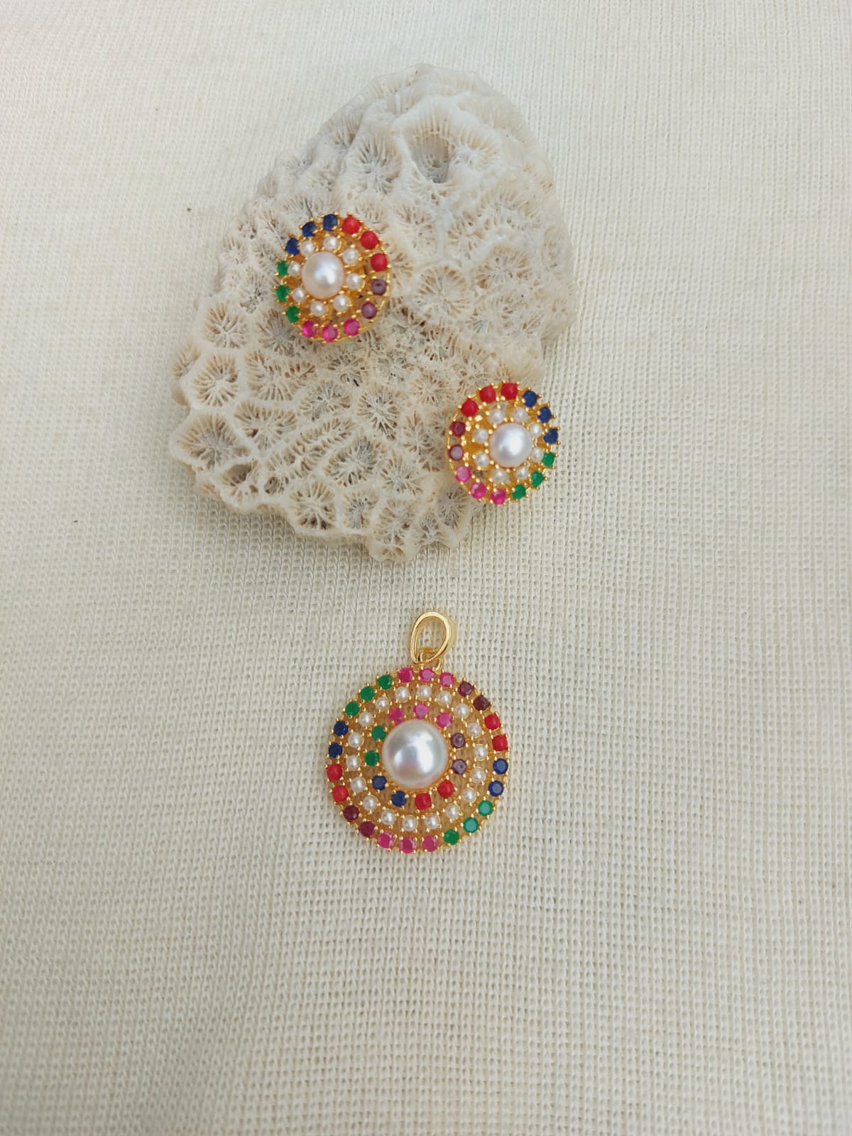 Multicolored gemstone-encrusted pendant set on textured fabric background, Mugdha Jewellery Store's Navaratna Pendant Set without Chain.