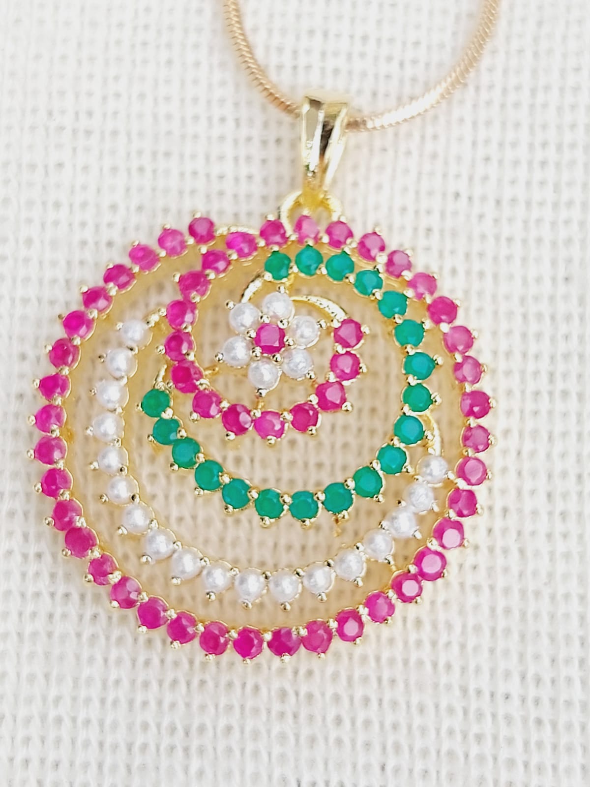Colorful spiral pendant with vibrant pink and turquoise crystals set in a gold-toned metal frame, displayed on a white background.