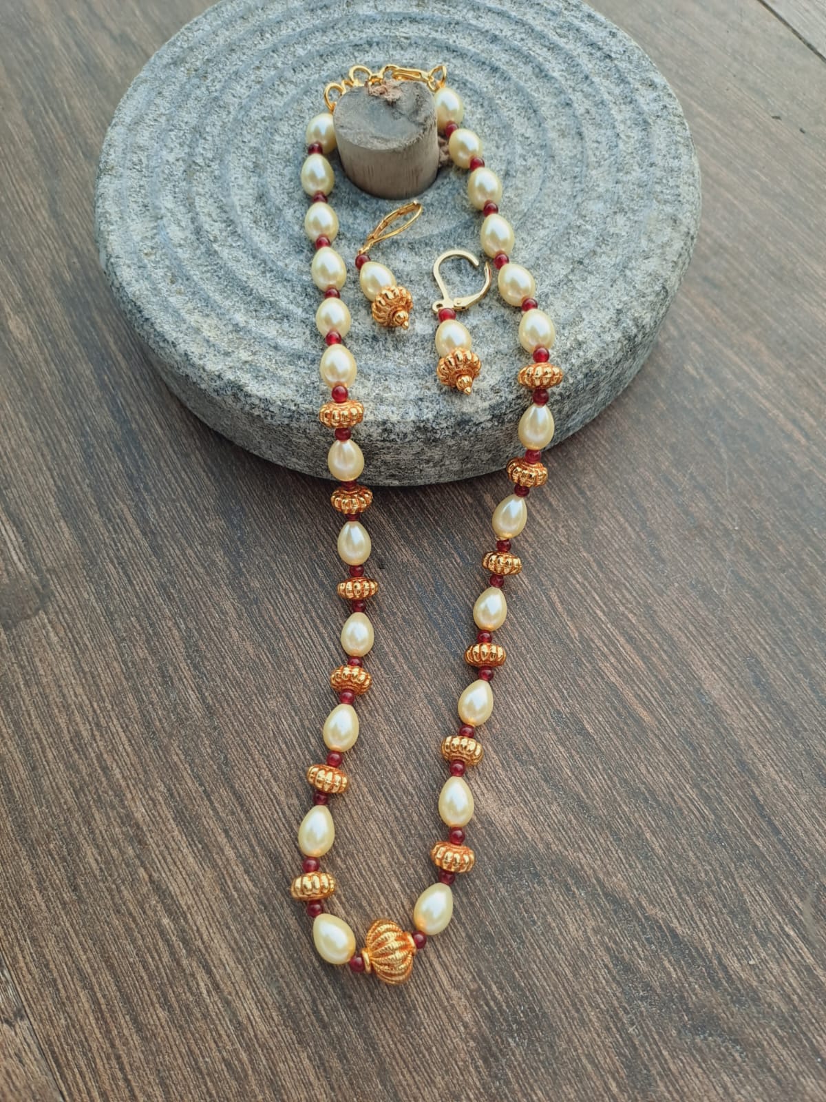 Elegant Oval Pearl Bead Set
Intricate necklace with oval-shaped pearls and ornate golden beads arranged in a cascading design, displayed on a natural stone surface.