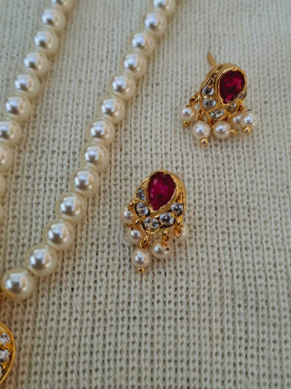 Elegant single pendant pearl set with delicate ruby-colored stones and sparkling accents, displayed on a beige knitted fabric.