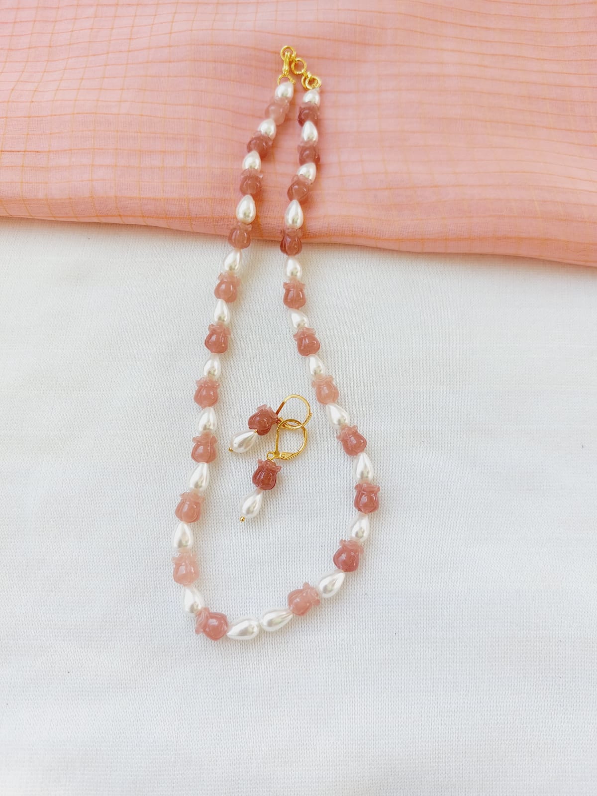 Elegant rose-shaped beads and pearl necklace with golden accent on a light pink fabric background.