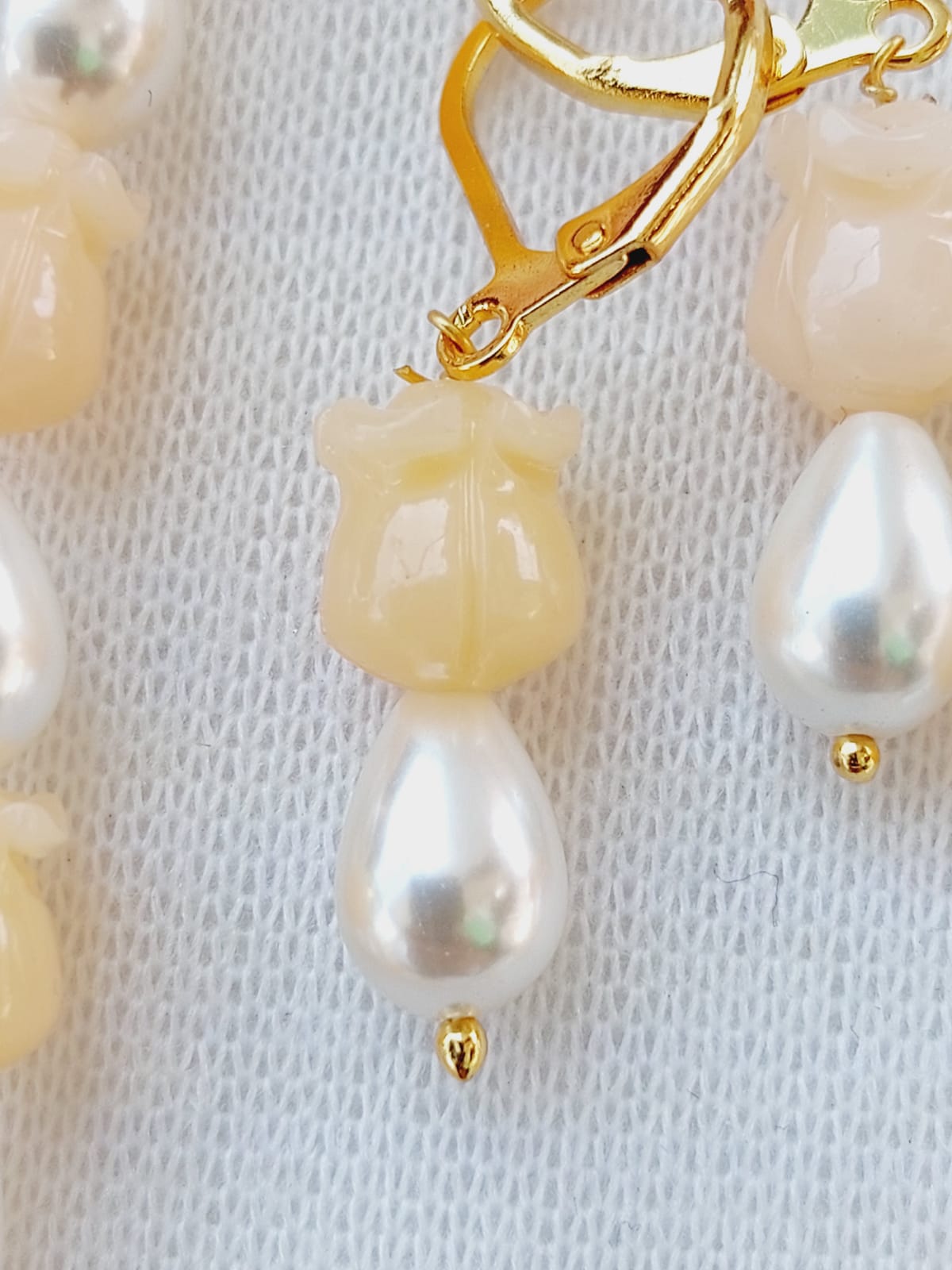 Elegant rose-shaped beads and pearl set in light yellow displayed on a textured white background