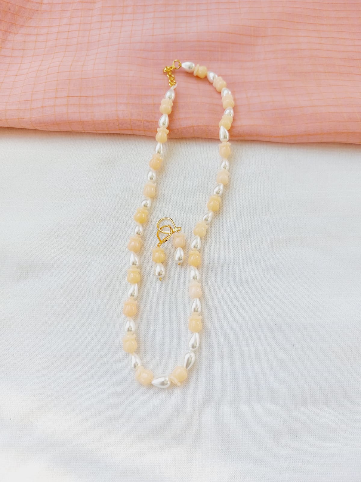 Elegant pearl and bead necklace with a golden clasp, displayed on a light pink and white background.