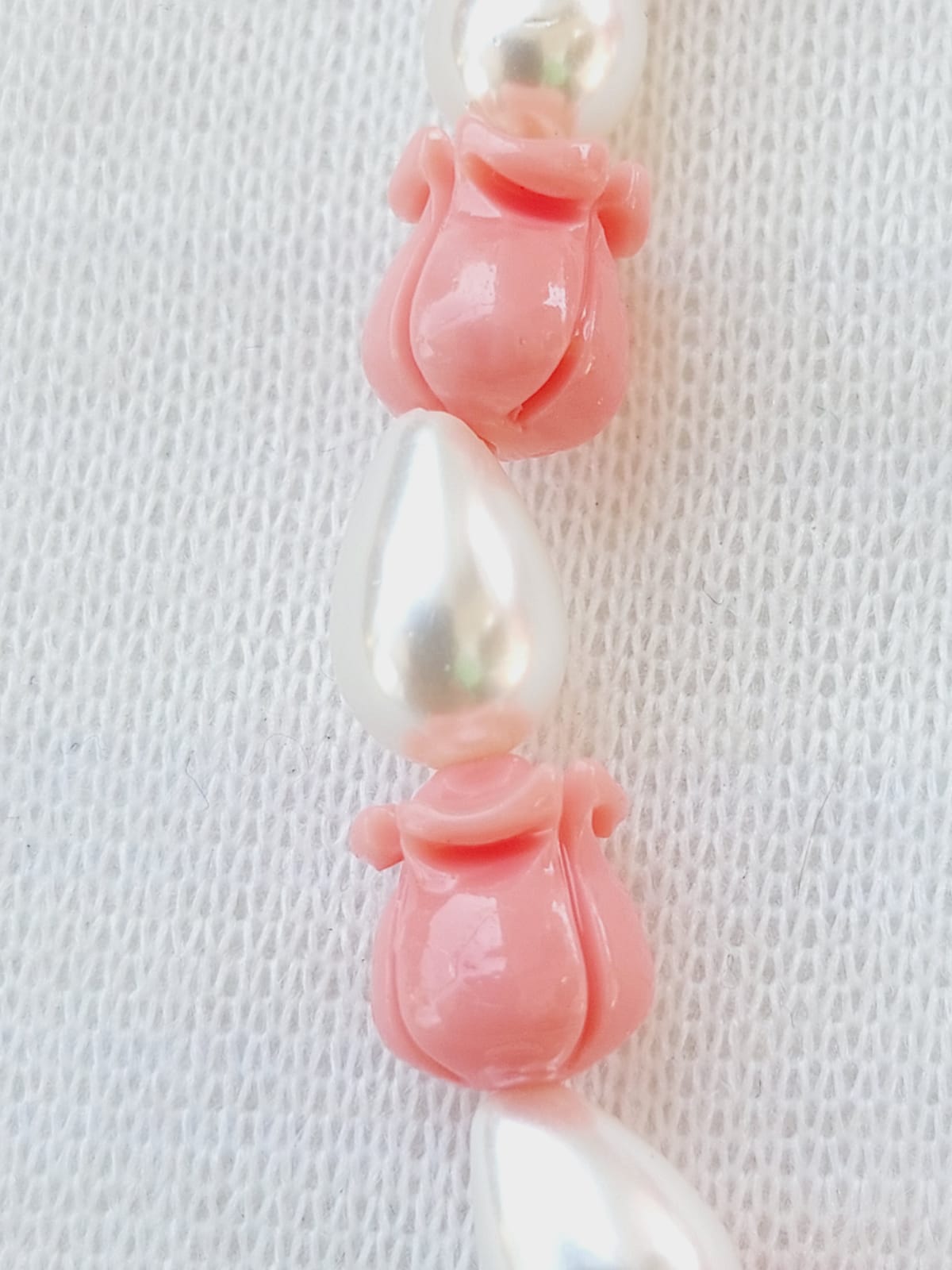 Rose-shaped beads and pearl set in pink tone on a textured background.
