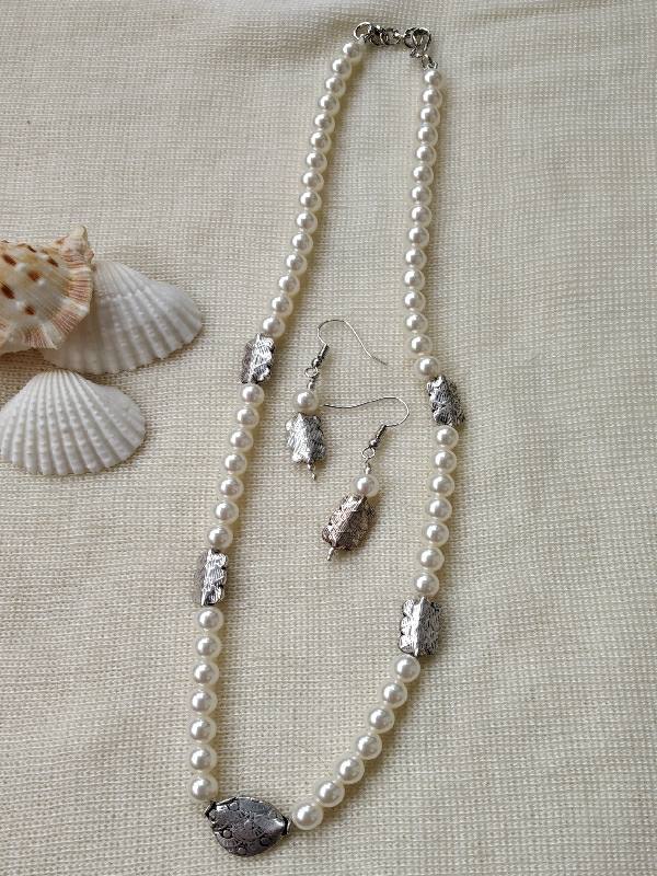 Elegant pearl necklace and earrings set with natural shell accents, placed on a textured cream background with seashells.