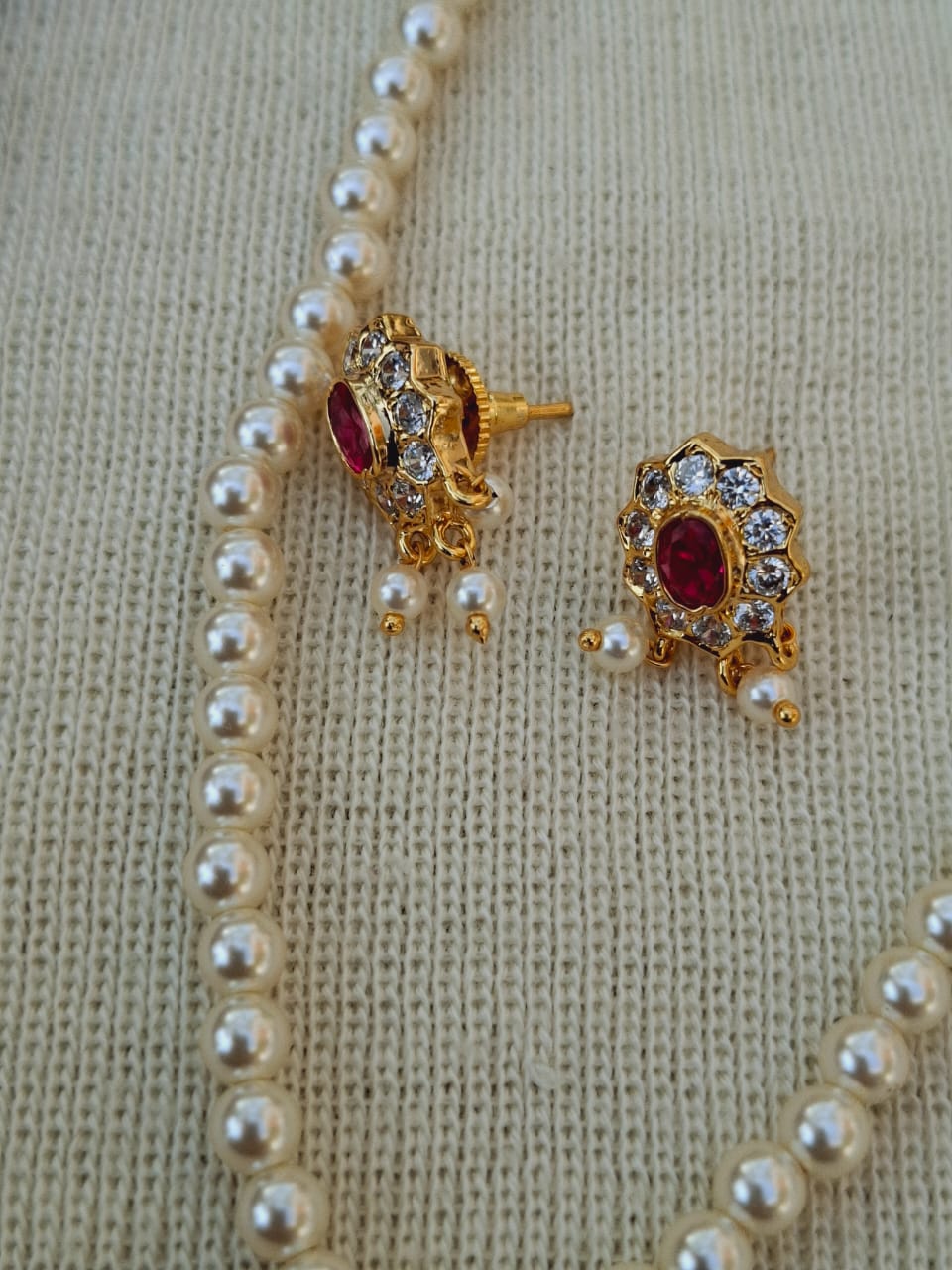 Elegant pearl necklace with ornate gold-tone pendant featuring a floral design accented by sparkling crystals and a vibrant red gemstone.