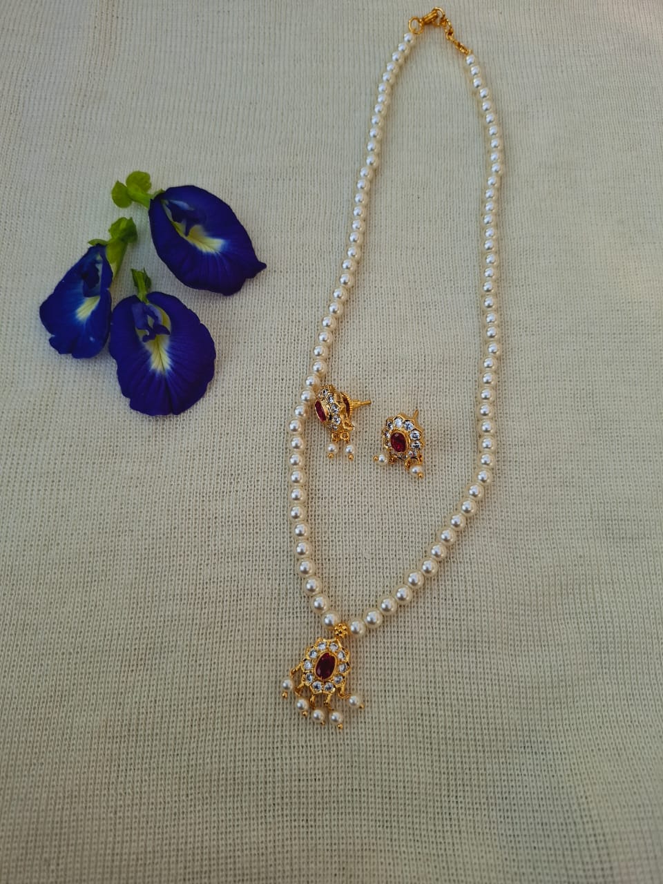White pearl necklace and earrings with flower-shaped gold and gemstone accents, displayed alongside blue iris flowers