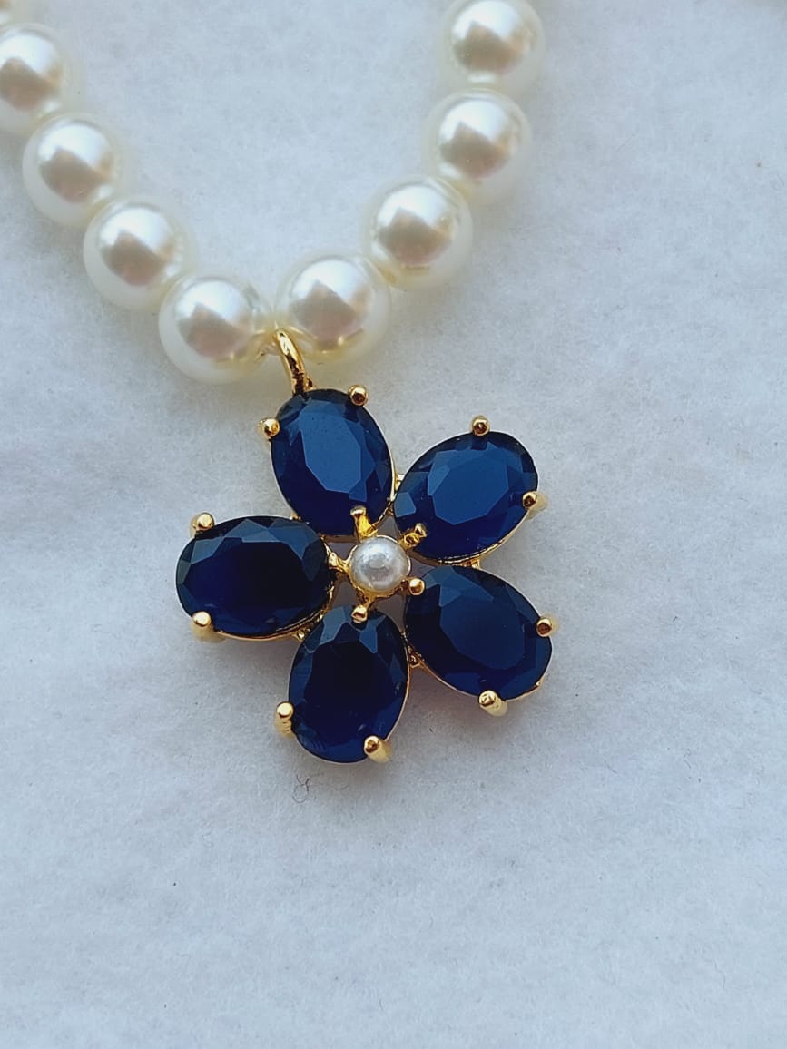 Elegant pearl necklace with navy blue gemstone flower pendant displayed on a light background