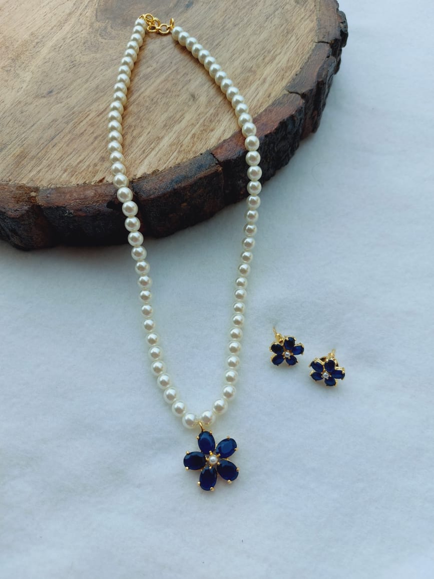 Elegant pearl necklace and earrings set with blue floral motifs on a wooden background
