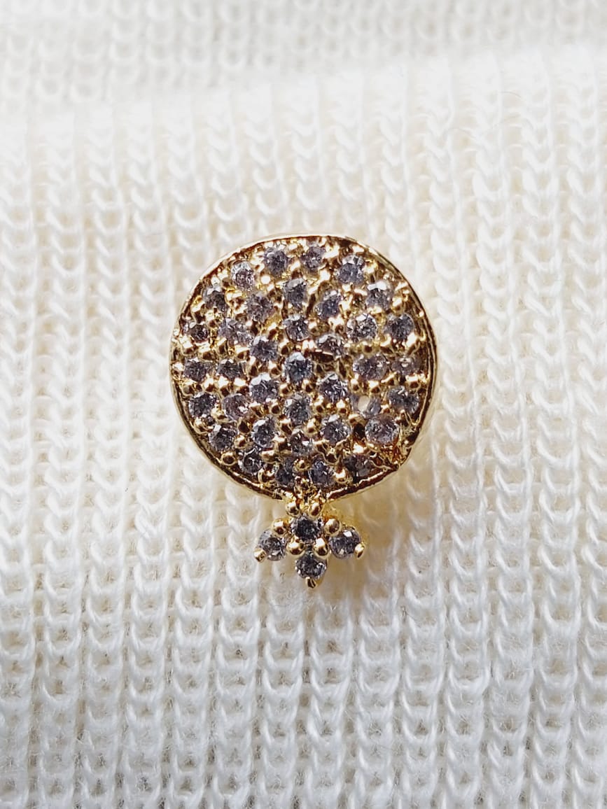 Sparkling round gold-tone earring decorated with clustered rhinestones, displayed on a white knitted fabric background.