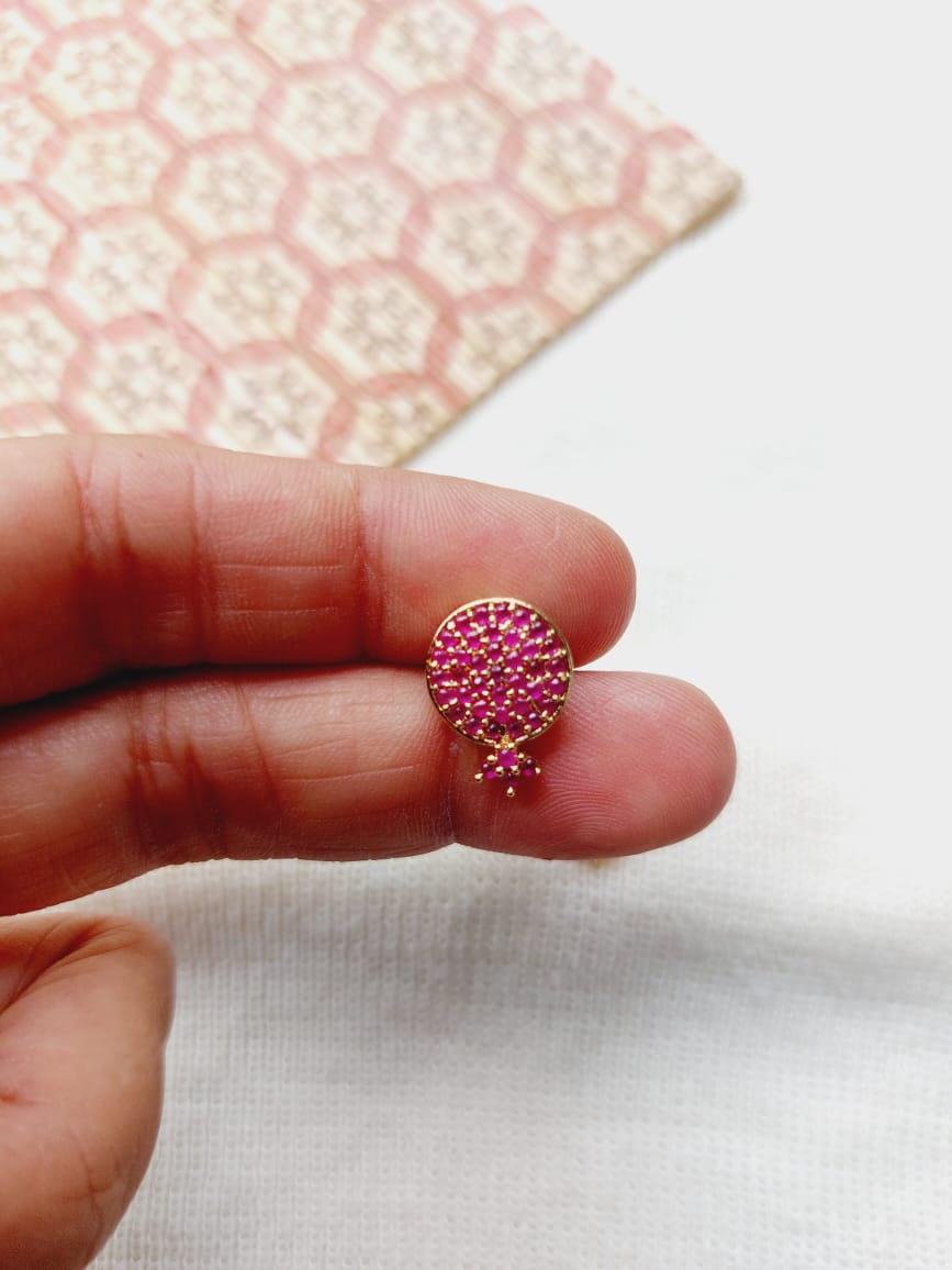 Dark pink bejeweled stone earring on a hand against a white and pink honeycomb pattern background from Mugdha Jewellery Store.