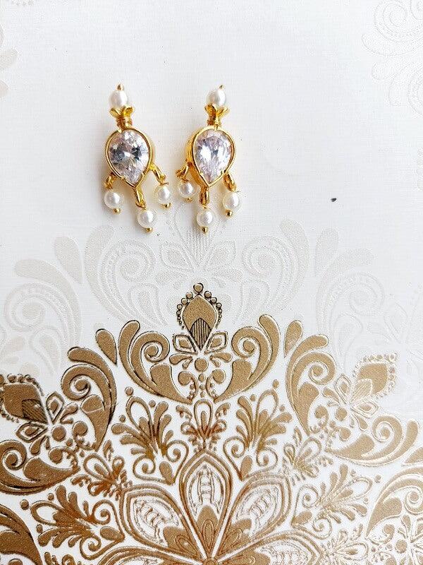 White stone tanmani earrings with gold-toned metal and pearl accents on white patterned background