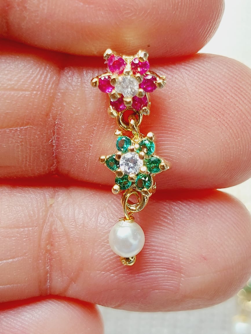 Sparkling floral earrings with vibrant gemstones and a delicate pearl accent, showcased on a hand.
