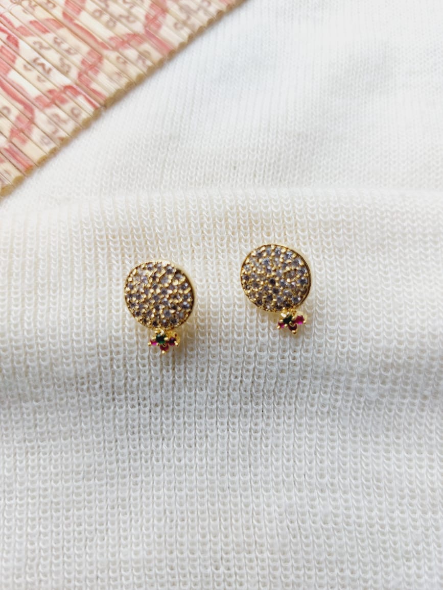 Elegant gold-tone round earrings adorned with sparkling multicolored stones, resting on a white fabric background.
