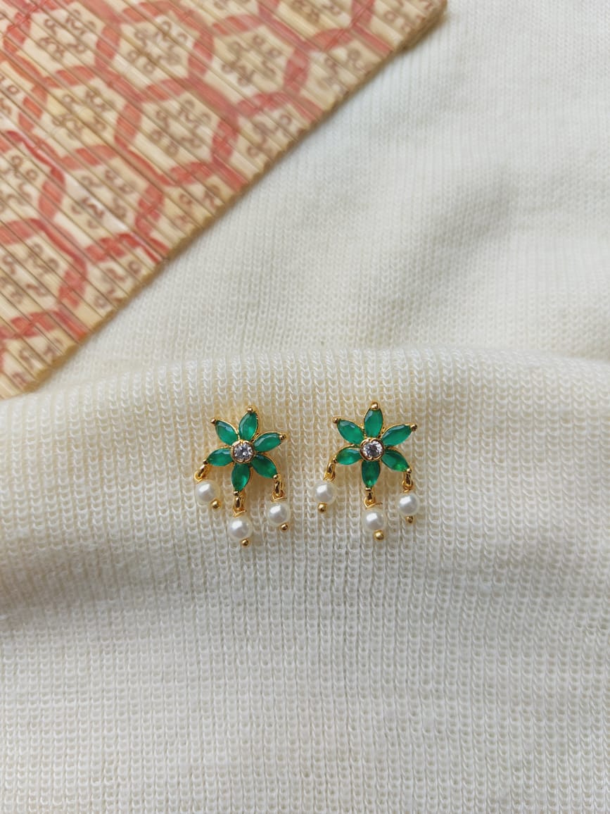 Elegant green stone star flower stud earrings with pearls, showcased on a light fabric background with a patterned textile.