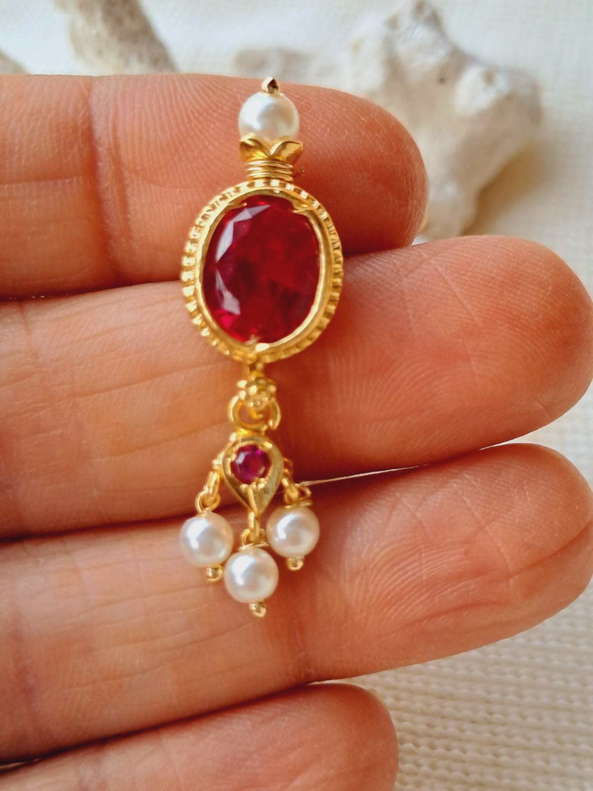 Elegant oval ruby pendant with pearl accents, showcased on a hand against a soft background.