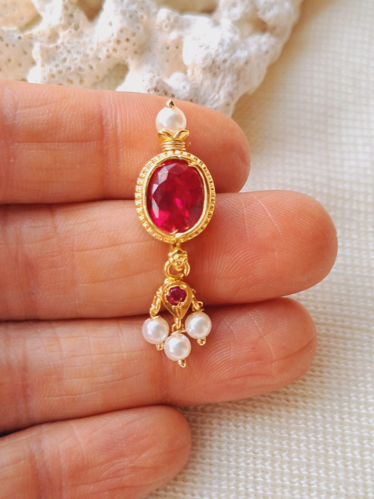 Dark pink stone danglers with pearl accents, held in a hand against a light background.