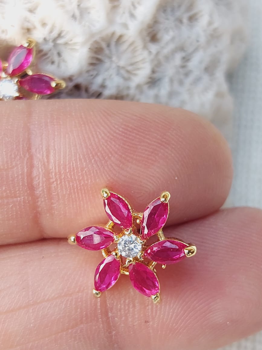 Dark pink stone star flower stud earrings on a hand against a soft, blurred background