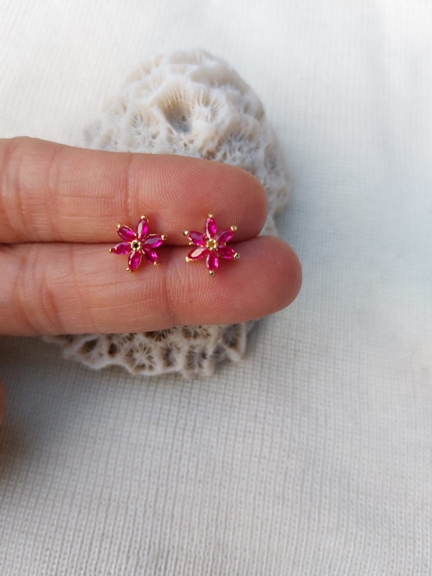 Dark pink stone star flower stud earrings from Mugdha Jewellery Store on a hand against a light background.