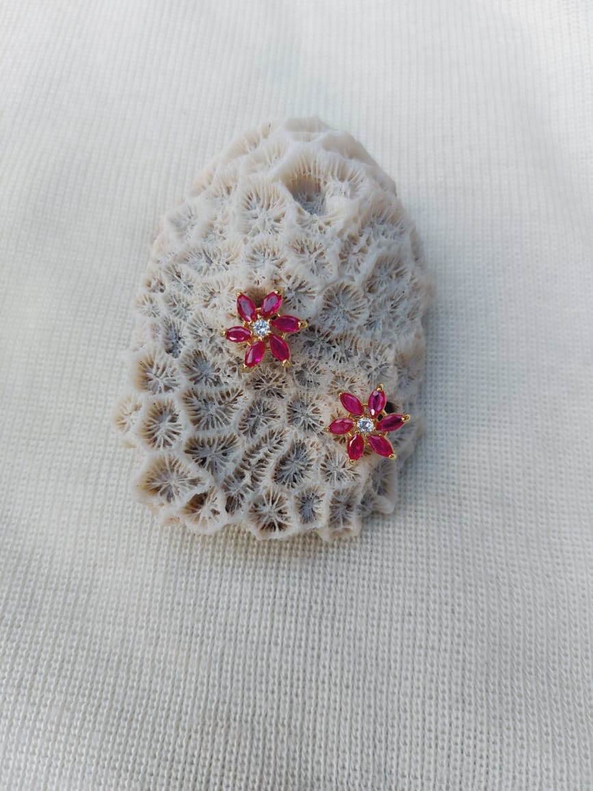 Dark pink stone star flower stud earrings resting on a light gray backdrop.