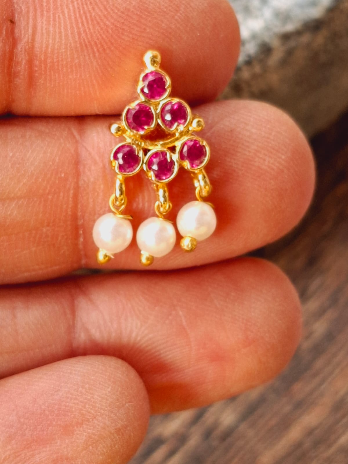 Dark pink floral-shaped Puneri earrings with pearl dangles, showcased on a hand.