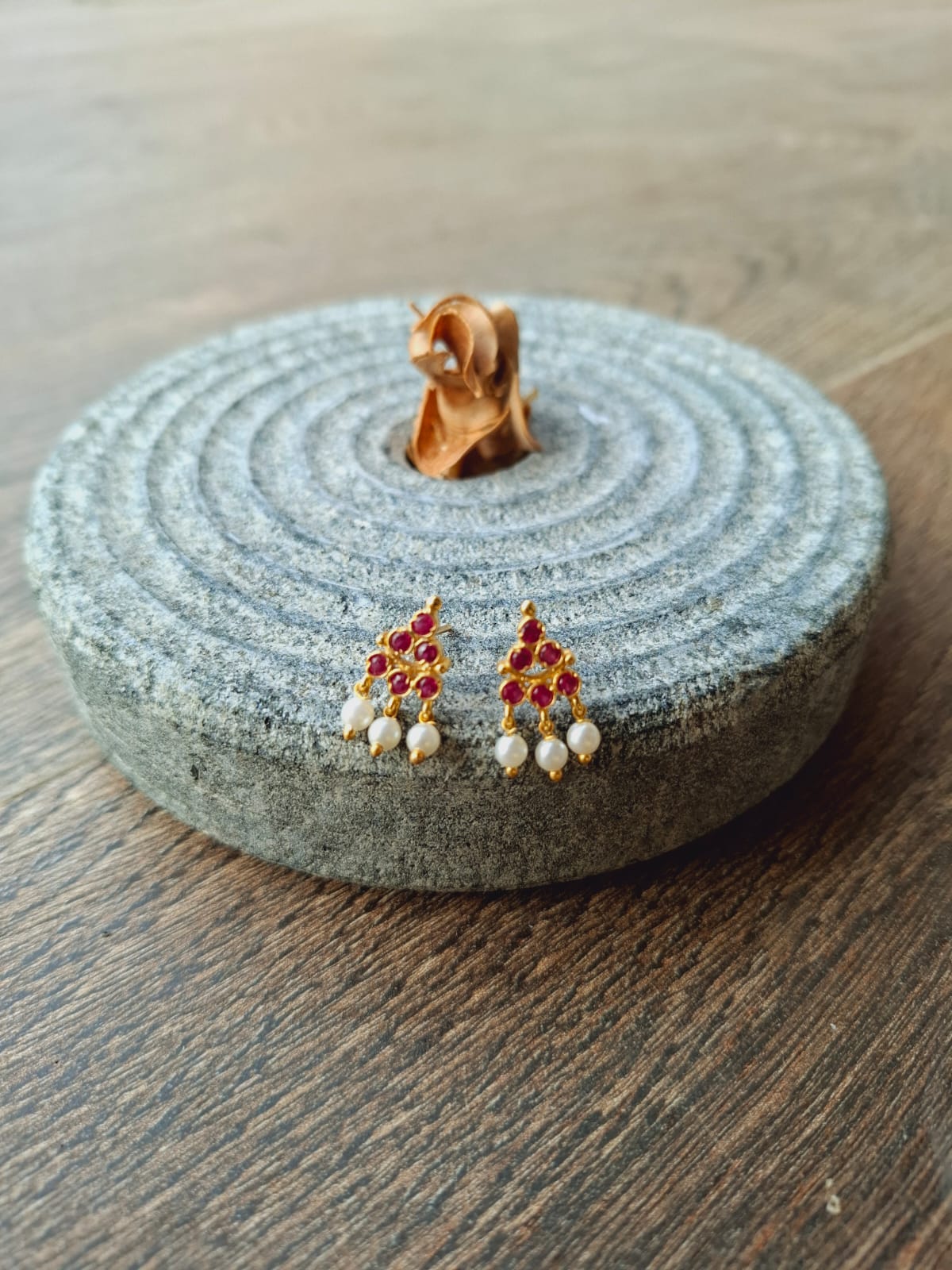 Dark pink Puneri earrings from Mugdha Jewellery Store displayed on a circular gray stone base with intricate patterns.