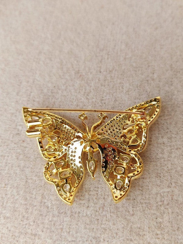 Elegant gold-toned butterfly brooch with intricate details and sparkling accents, showcased on a light-colored background.