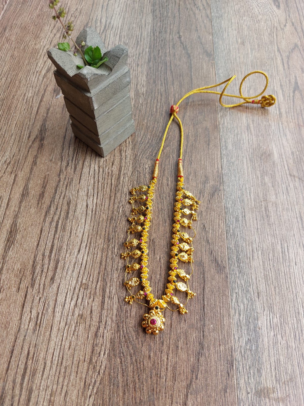 Colorful Dholki Bead Necklace - Detailed multicolored Kolhapuri saaj short necklace with beads, displayed on a wooden surface alongside a potted plant.