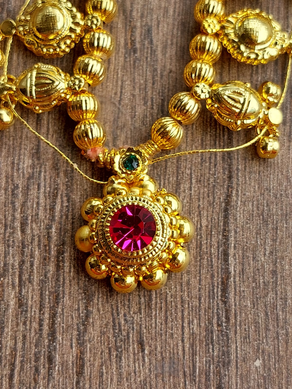 Intricate golden beaded necklace with vibrant red gemstone centerpiece, displayed on a rustic wooden surface.