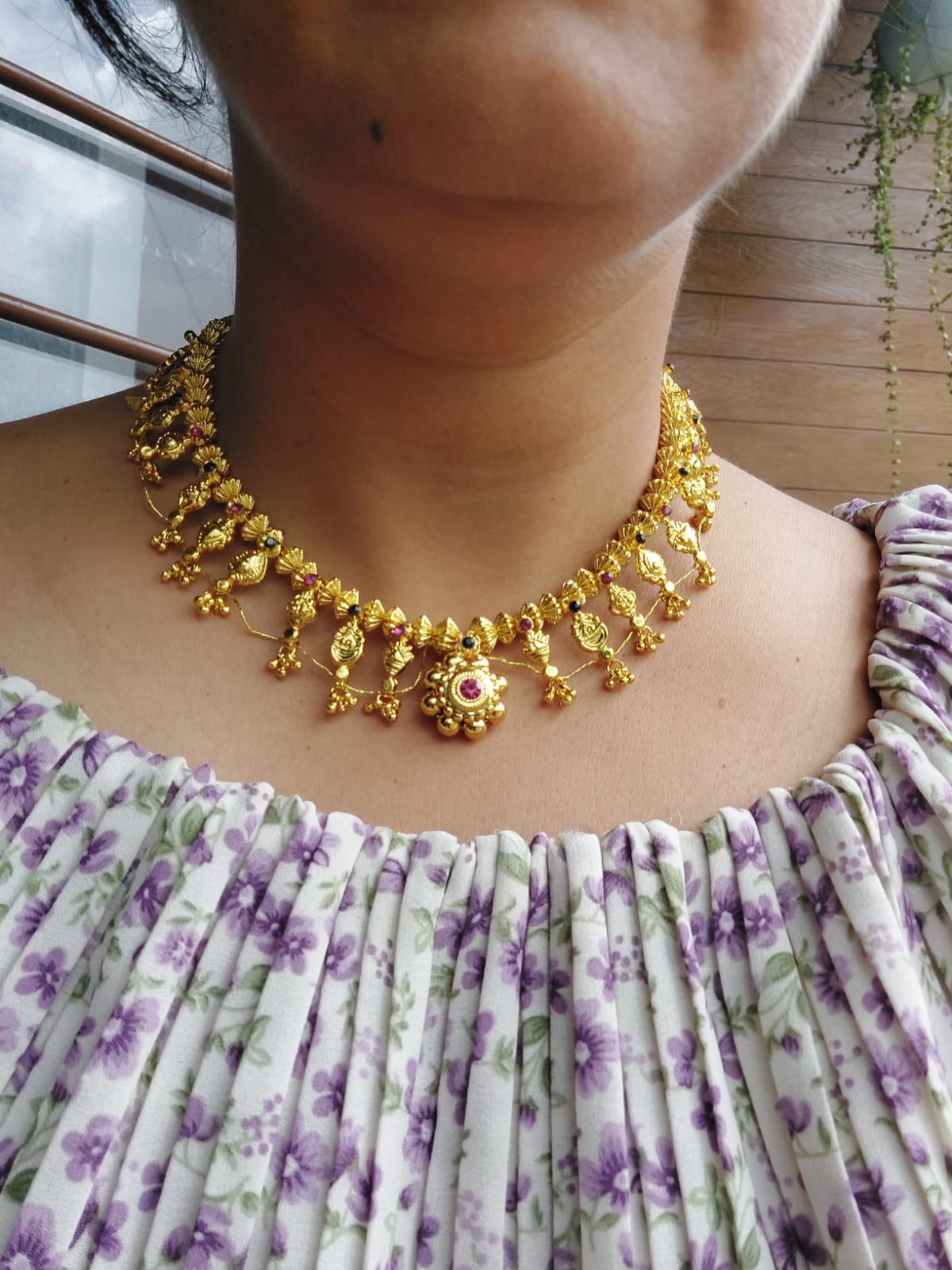 Decorative gold-toned necklace with bead and pendant accents, worn by a person in a floral patterned top