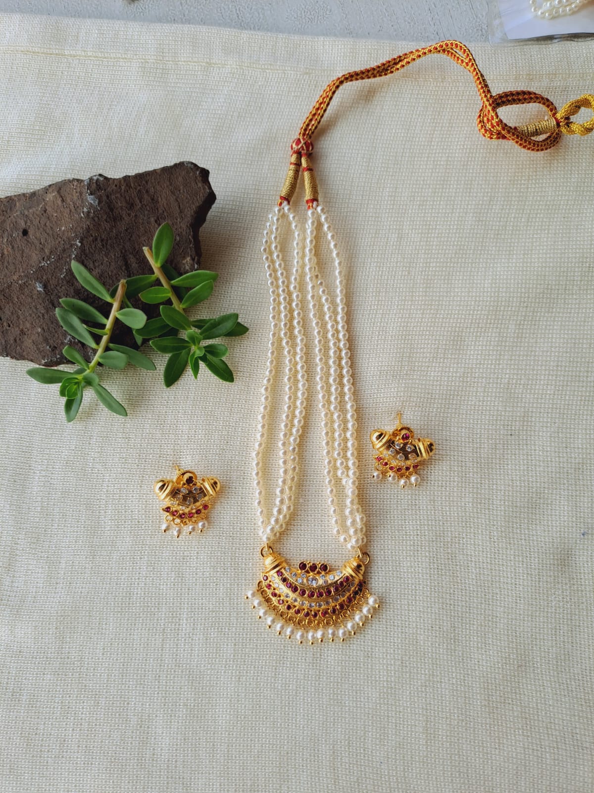 Small gold-toned chandrakor karwari tanmani necklace with pearl and bead accents displayed on white textile with natural foliage
